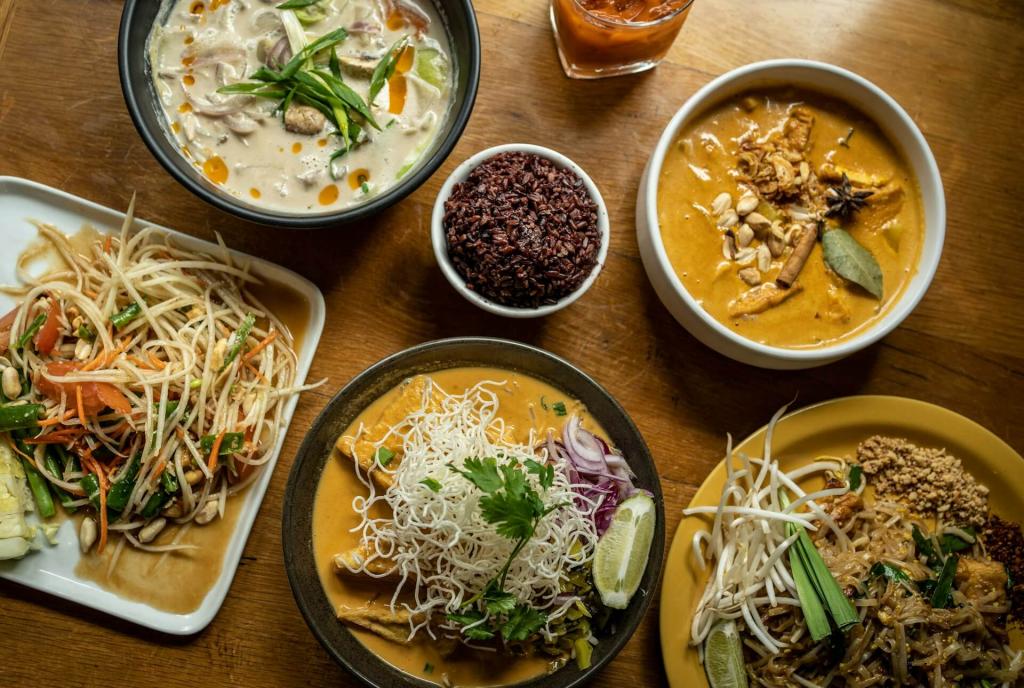 Verschiedene Thailändische Suppen und Gerichte wie Khao Soi in Tellern und Schalen angerichtet auf einem Holztisch.
